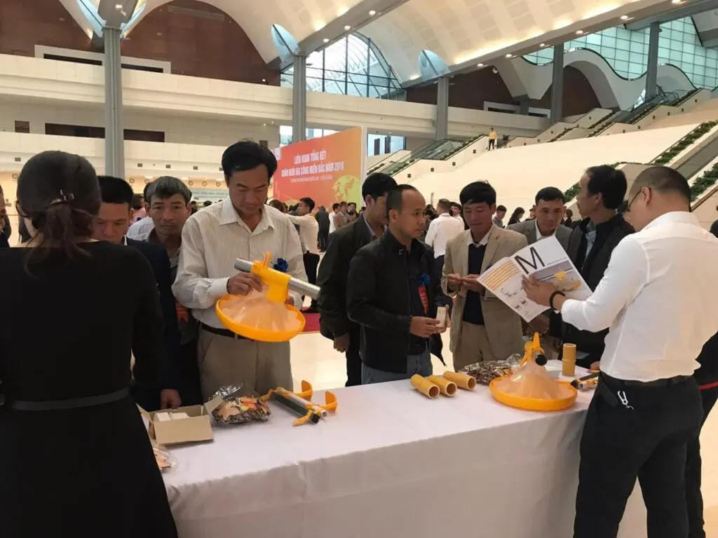 Industry professionals examine LANDMECO yellow pan feeding systems for broilers at a poultry trade show.