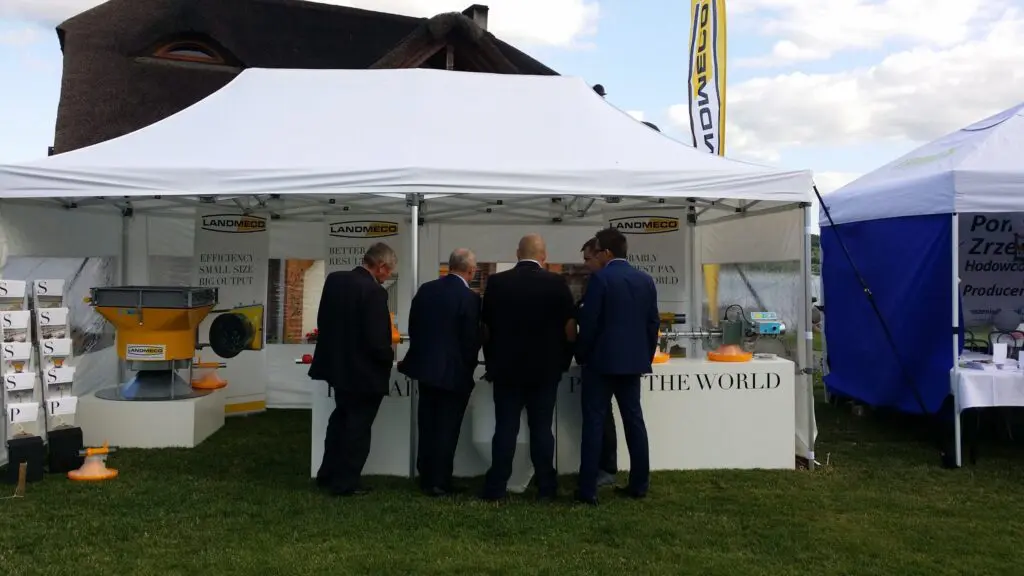 LANDMECO experts at a trade show booth demonstrating automated pan feeding systems and poultry farming equipment.
