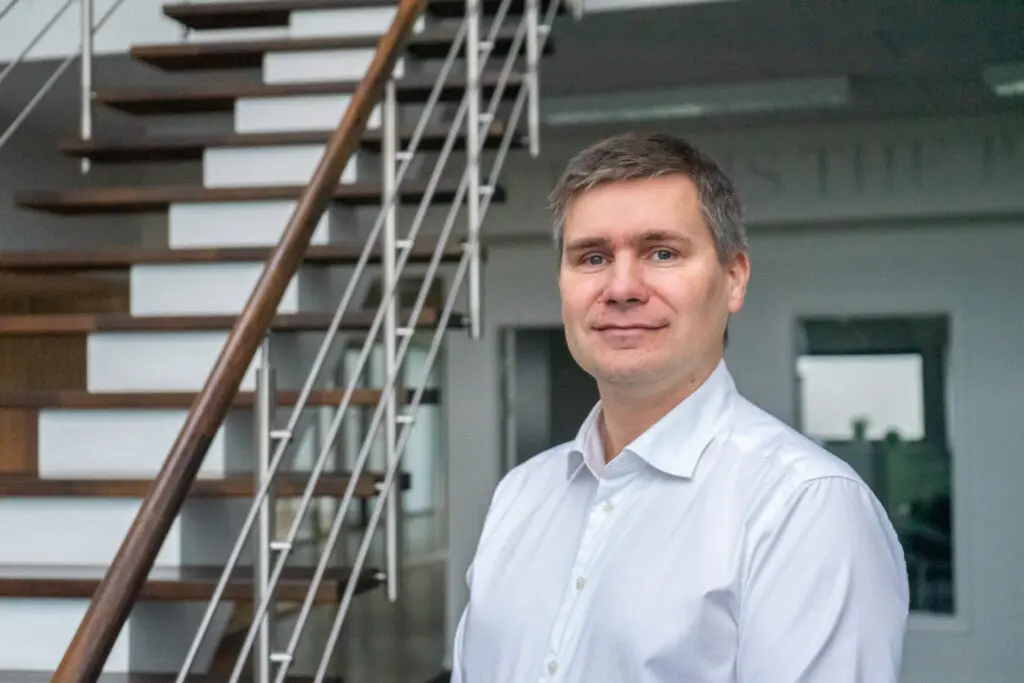 Professional LANDMECO team member in a white shirt standing in front of an office staircase in Ølgod, Denmark.