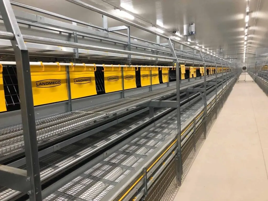 LANDMECO aviary system featuring metal tiers and yellow nesting flaps for cage-free poultry production.