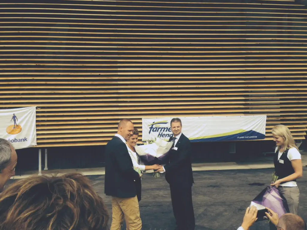 LANDMECO partners receiving flowers at a farming event with Rabobank and ForFarmers Hendrix banners in the background.