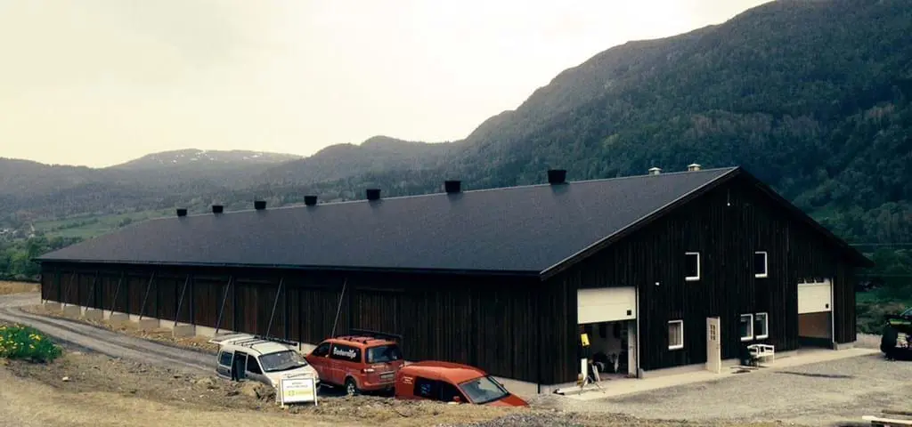 Modern dark wood poultry house with roof vents in a mountainous landscape, showcasing LANDMECO equipment.