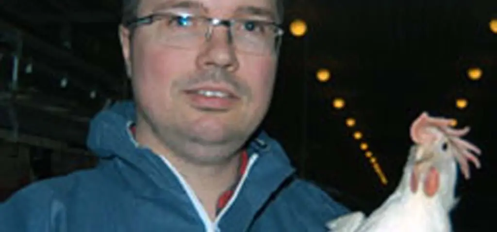 Landmeco Aasen holding a white hen, demonstrating poultry welfare in a professional farming environment.