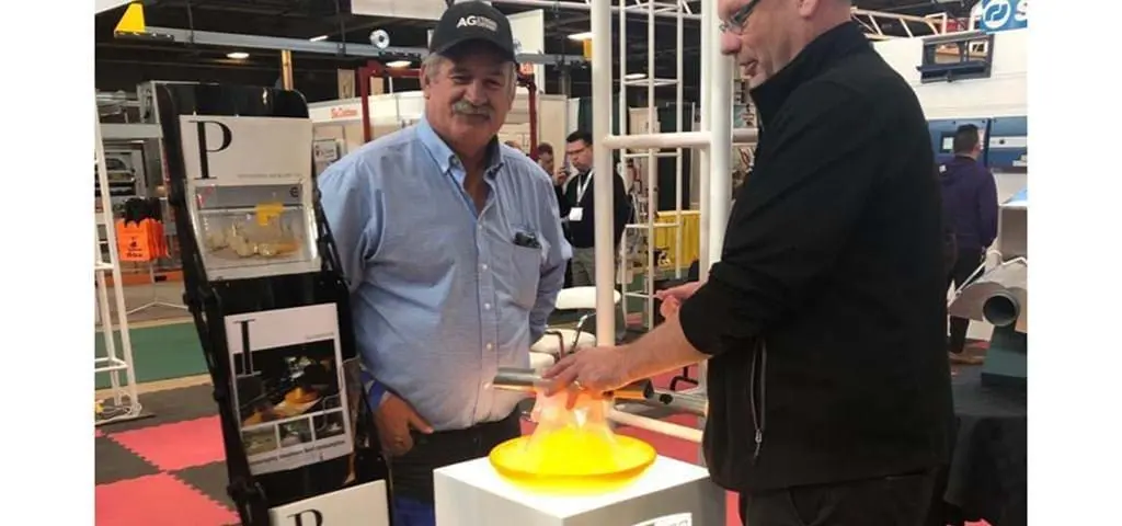 LANDMECO representatives demonstrating a yellow poultry pan feeding system at a trade show booth.