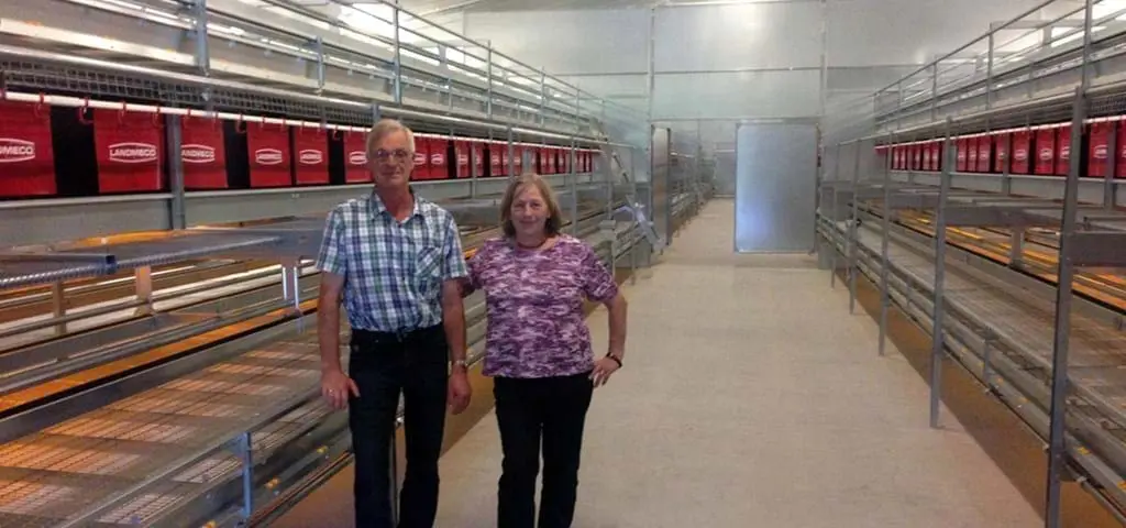 Man and woman in a poultry house with LANDMECO tiered aviary systems for cage-free egg production.
