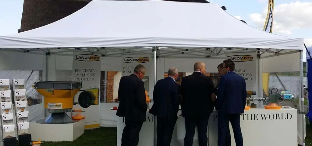Professionals at a LANDMECO trade show booth inspecting automated poultry feeding systems and broiler equipment.