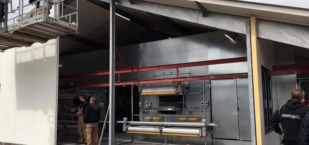 Technicians installing LANDMECO poultry aviary tiers in a new commercial house for efficient egg production.