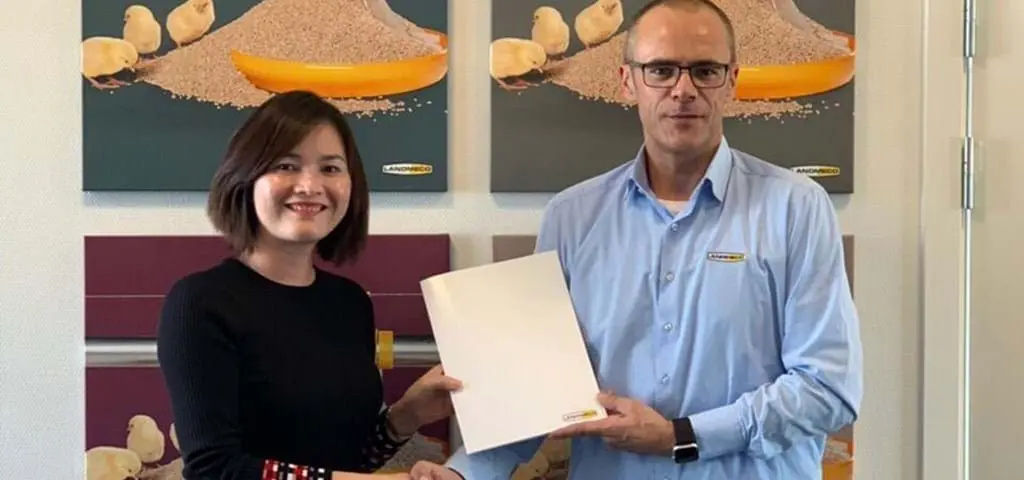LANDMECO representatives hold a folder to celebrate the first order in Vietnam in front of poultry equipment posters.