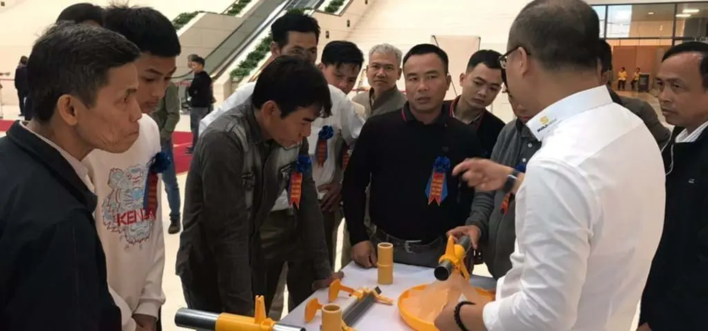 Professionals examining LANDMECO's Kick-off broiler pan feeding system at a poultry equipment demonstration.