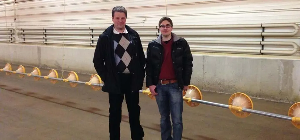 Two experts standing next to a LANDMECO automated broiler pan feeding system in a modern poultry house.