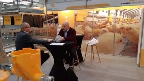 Professionals discussing poultry systems at a SKIOLD LANDMECO booth with a chick mural and feeding equipment.