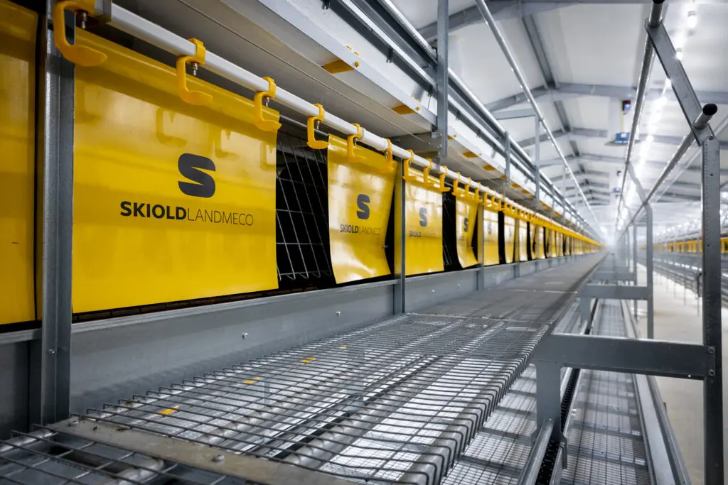 Yellow SKIOLD LANDMECO integrated chicken nests in a modern, automated aviary system for layers.