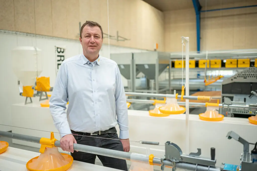 Landmeco CEO Anders Kristian Andersen with yellow pan feeding systems in a poultry equipment production hall.