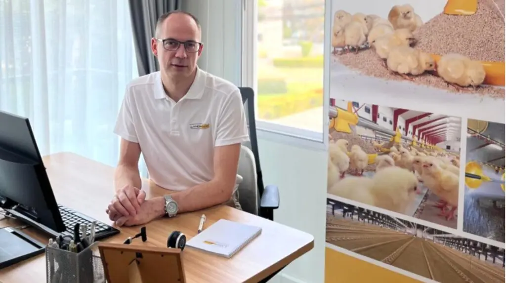 Frank Andreasen of LANDMECO at his desk, featuring poultry house and chick equipment graphics.
