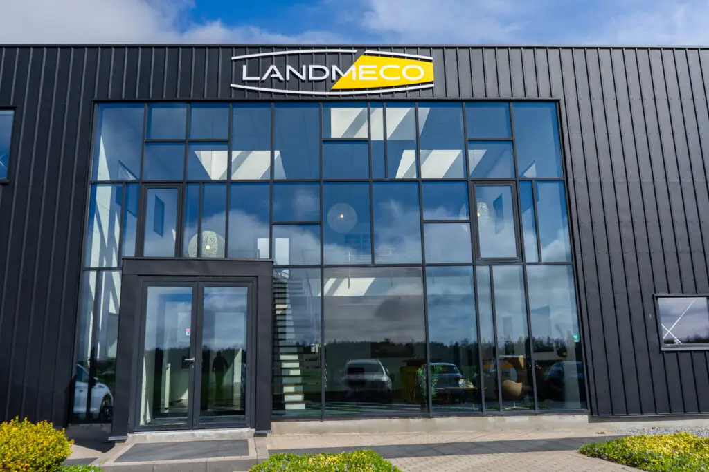 LANDMECO headquarters building in Ølgod, Denmark, featuring a modern glass facade and company logo on a black metal wall.