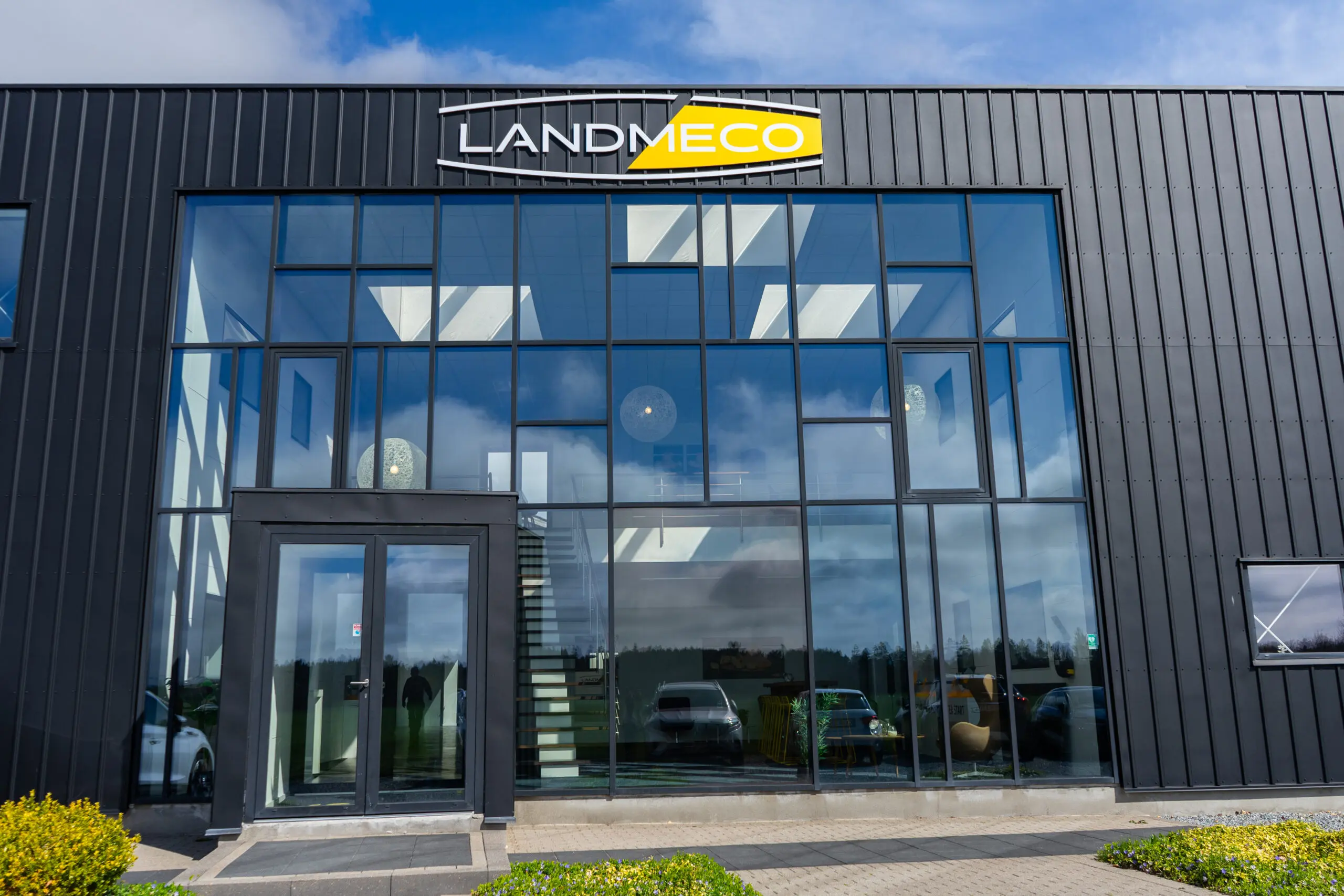 LANDMECO headquarters building in Ølgod, Denmark, featuring a modern glass facade and company logo on a black metal wall.