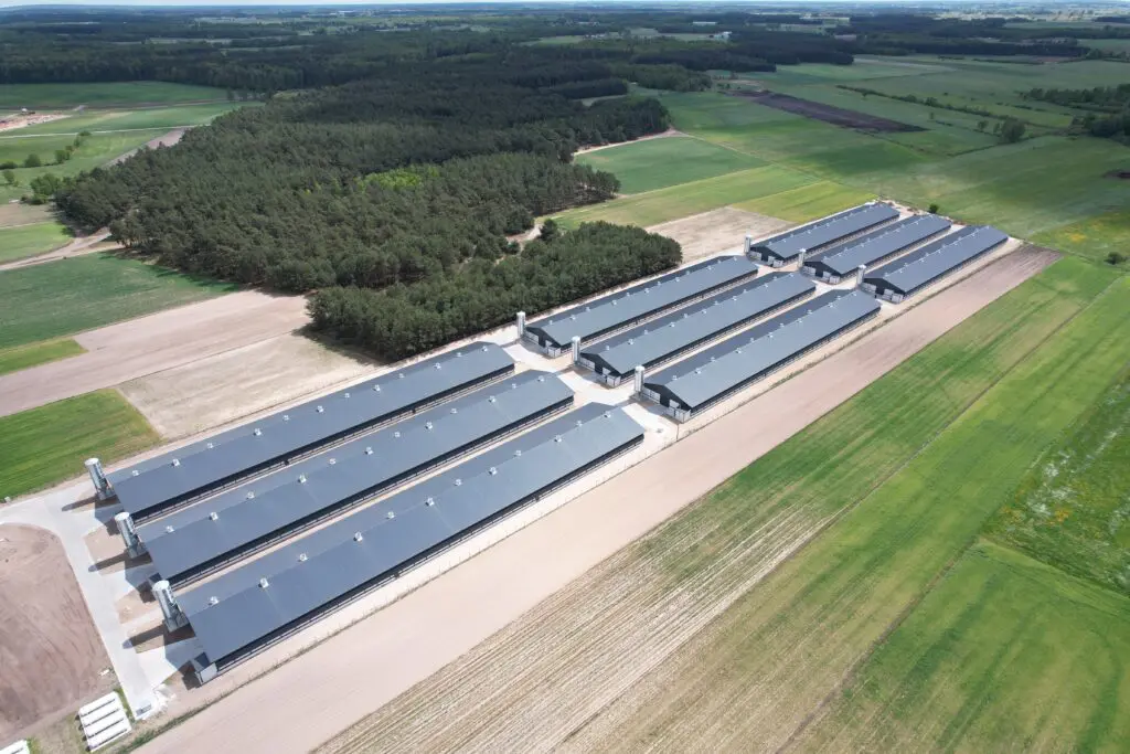 Aerial view of nine modern broiler poultry houses by LANDMECO in Żuromin, Poland, surrounded by farmland and forests.