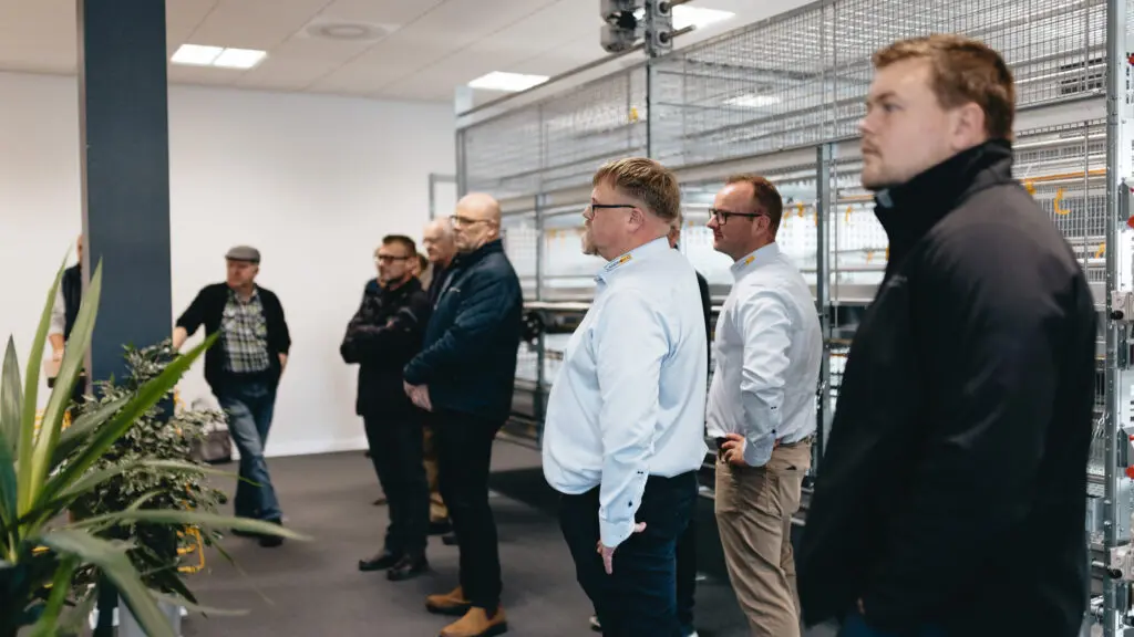 En gruppe mænd i et showroom kigger på LANDMECOs moderne staldsystemer til fjerkræ under Fjerkrædagen 2025.