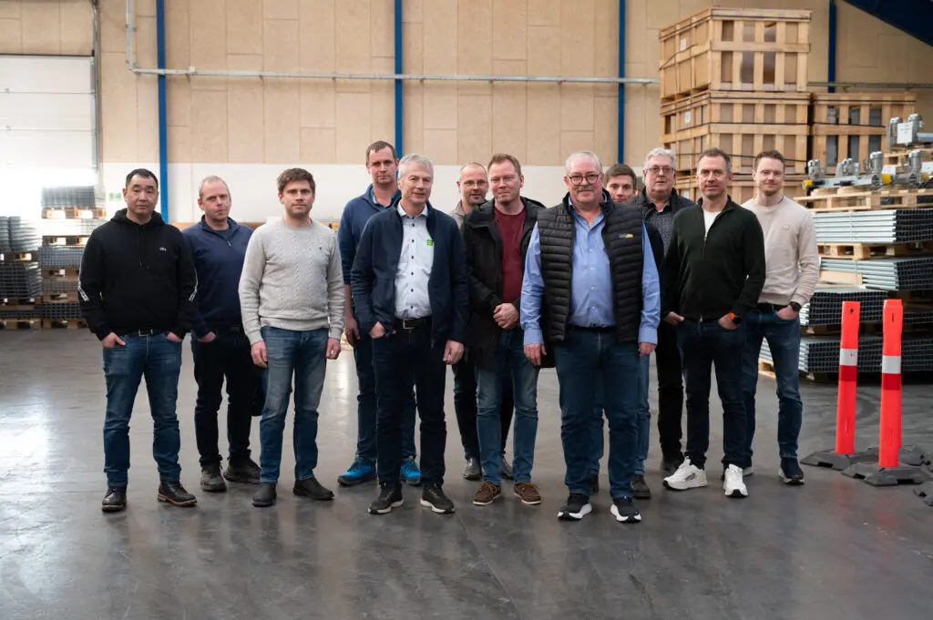 A group of professional men standing in a LANDMECO poultry equipment warehouse during a factory visit from Norway.