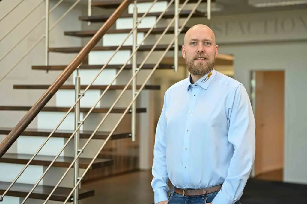 Mikael Hald, Area Sales Manager at LANDMECO, standing in a professional office in front of a modern wooden staircase.