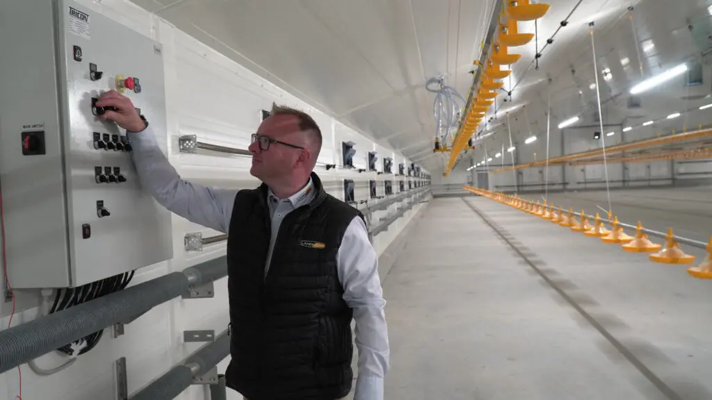 Morten Jakobsen fra LANDMECO ved kontrolpanel i en moderne slagtekyllingestald med gult fodringssystem.
