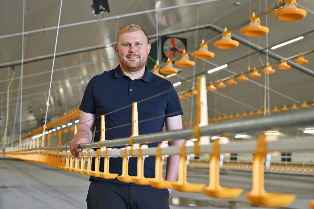 Mathias Højgaard står i sin nye, moderne kyllingestald i Vestjylland ved de gule fodringsanlæg.