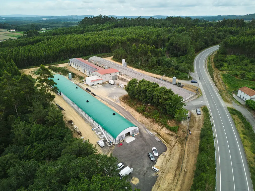 High-angle aerial shot of the Granxa Avícola O’Viso egg production facility in Arzúa, Spain, featuring farm buildings surrounded by forest.