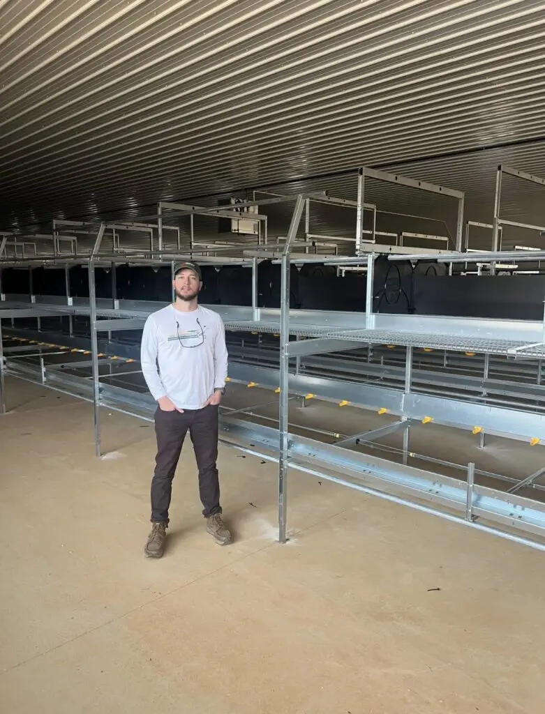 Jeromy Slayden standing in a modern poultry house with LANDMECO aviary equipment.