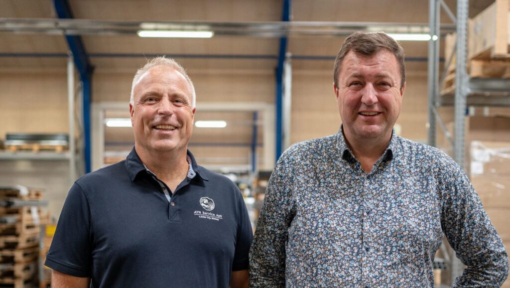 Mogens Hansen fra ATN Service og Anders Kristian Andersen fra LANDMECO smiler i en lagerhal.