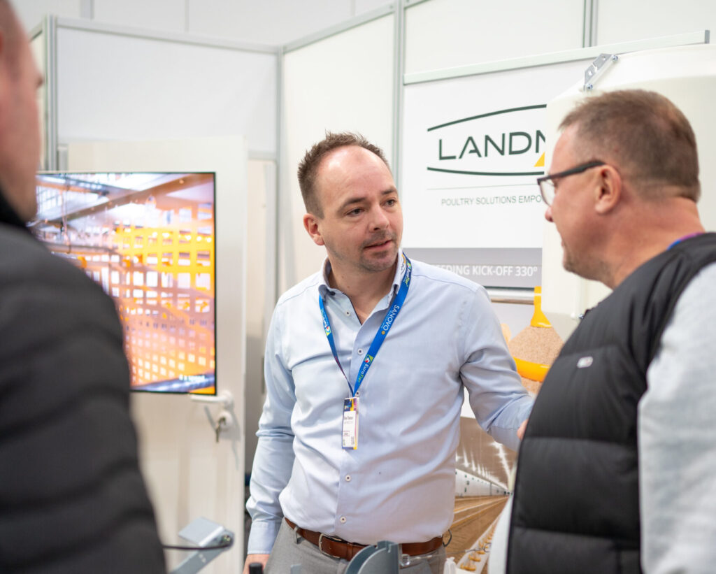 LANDMECO Sales Manager discussing poultry equipment with producers at a trade show.