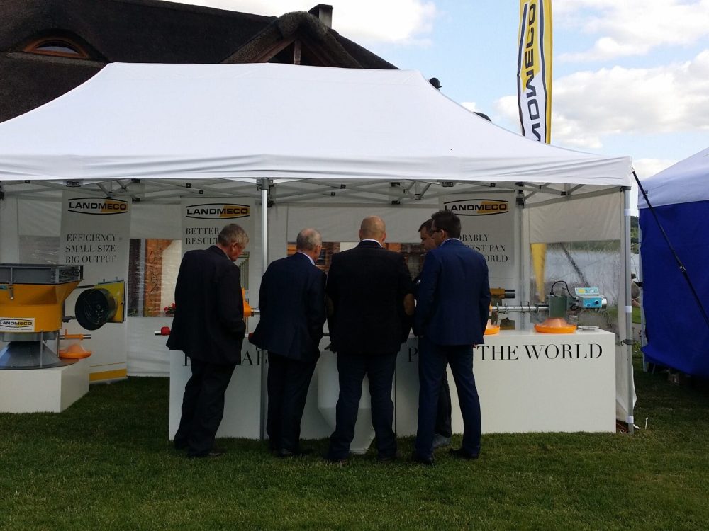 LANDMECO experts at a trade show booth demonstrating automated pan feeding systems and poultry farming equipment.