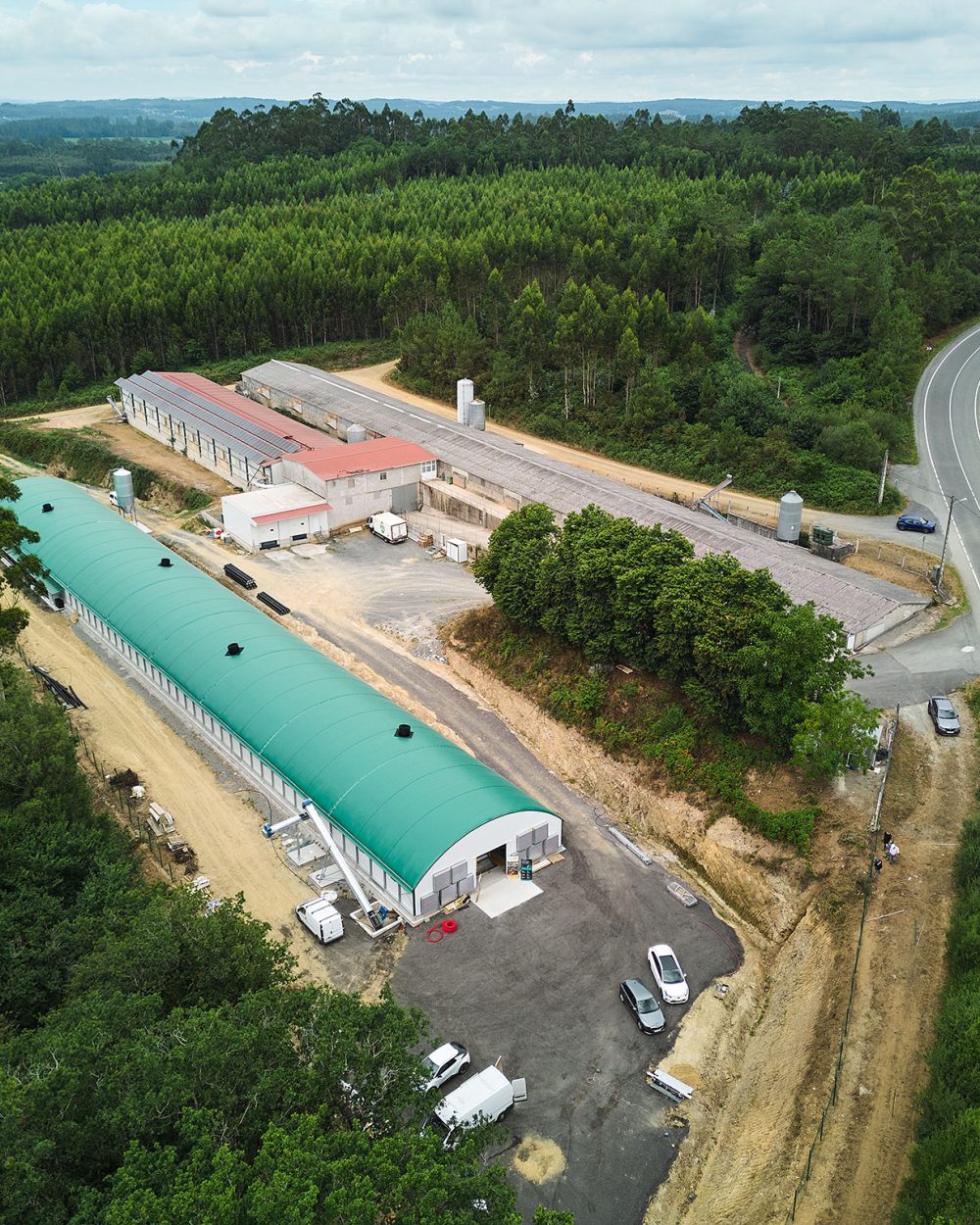 High-angle aerial shot of the Granxa Avícola O’Viso egg production facility in Arzúa, Spain, featuring farm buildings surrounded by forest.