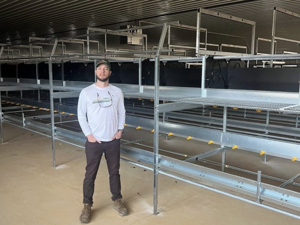 Jeromy Slayden standing in a modern poultry house with LANDMECO aviary equipment.