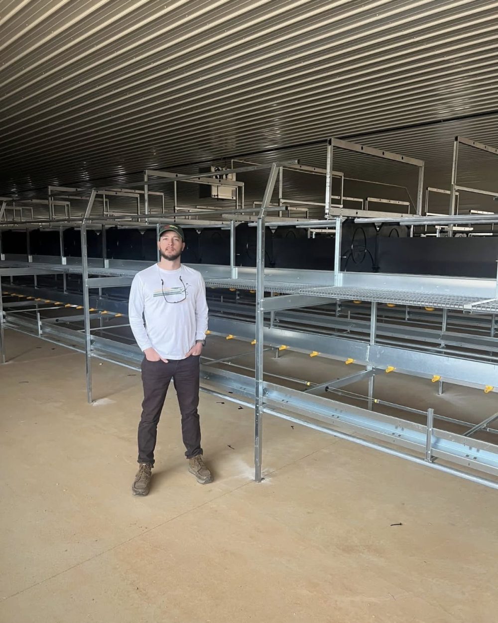 Jeromy Slayden standing in a modern poultry house with LANDMECO aviary equipment.