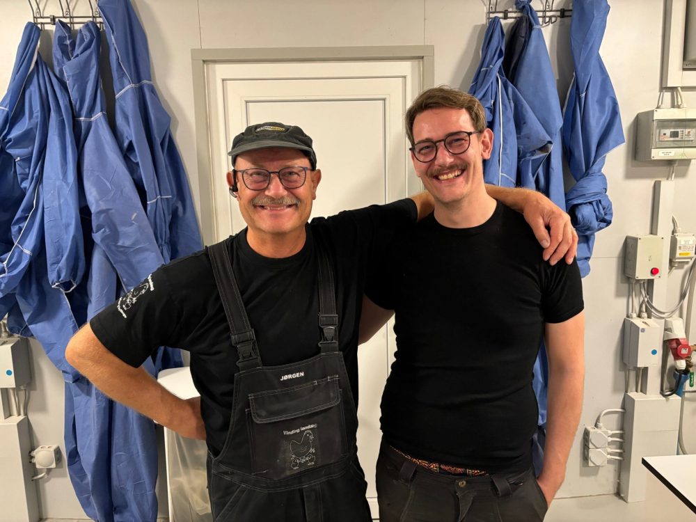 Jørgen Lodberg and his son in work gear, smiling at their Danish poultry facility featuring LANDMECO equipment.