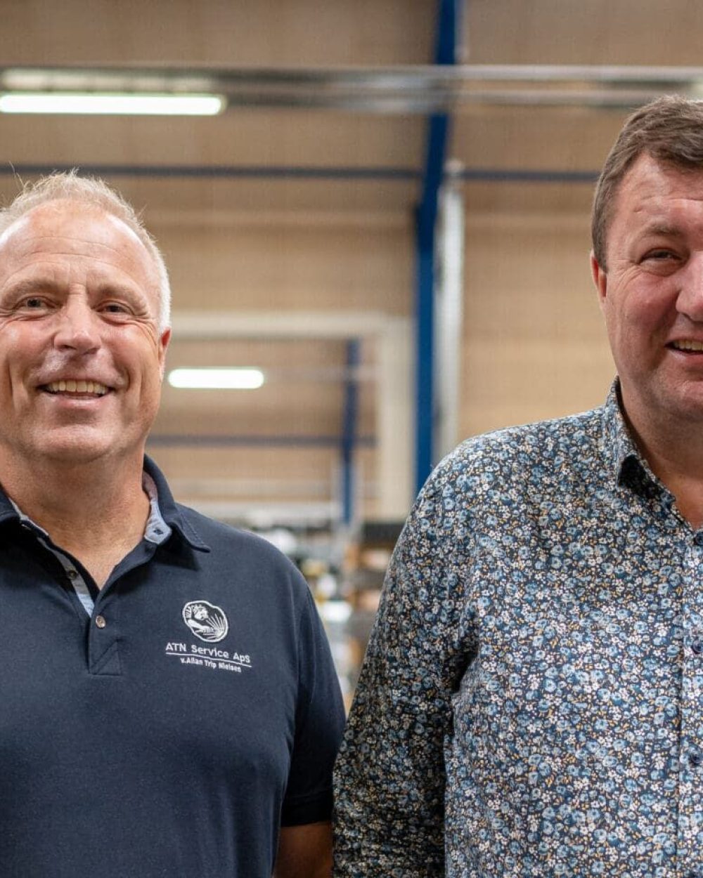 Mogens Hansen fra ATN Service og Anders Kristian Andersen fra LANDMECO smiler i en lagerhal.
