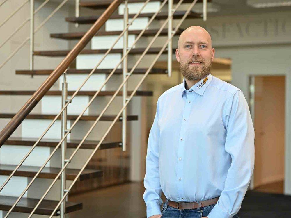 Mikael Hald, Area Sales Manager at LANDMECO, standing in a professional office in front of a modern wooden staircase.