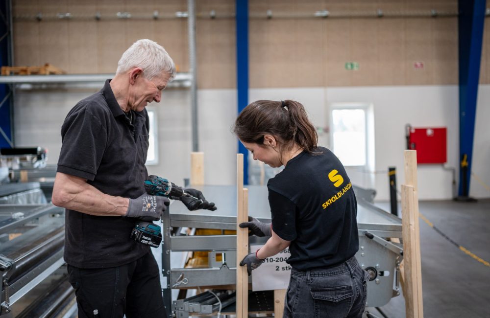 LANDMECO ESG: Sustainable Poultry Equipment Manufacturing LANDMECO employees in a warehouse assembling metal poultry system parts, highlighting ESG and social responsibility.