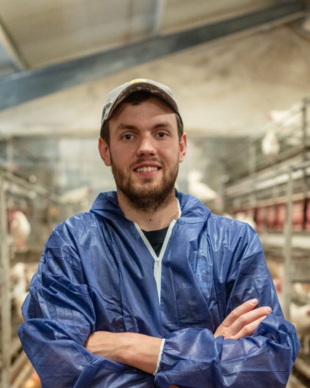 Danish farmer in a blue suit standing in a LANDMECO layer aviary system house with tiered poultry equipment.