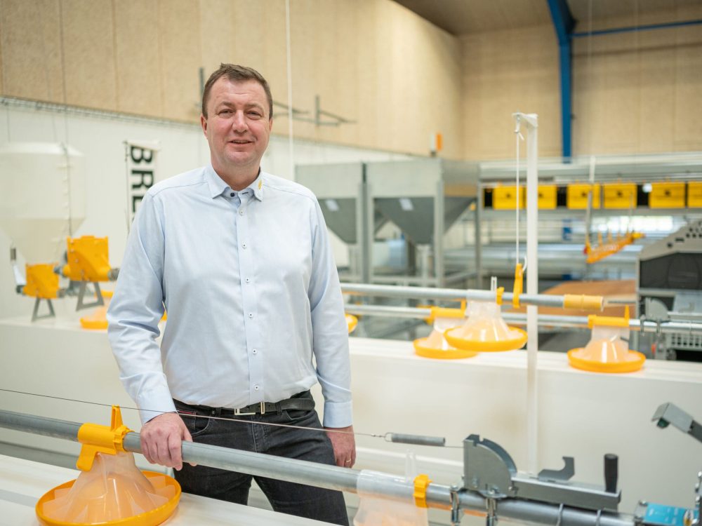Landmeco CEO Anders Kristian Andersen with yellow pan feeding systems in a poultry equipment production hall.
