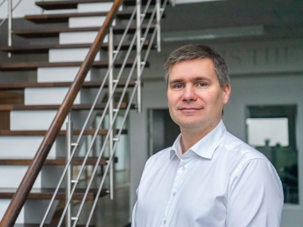 Professional LANDMECO team member in a white shirt standing in front of an office staircase in Ølgod, Denmark.