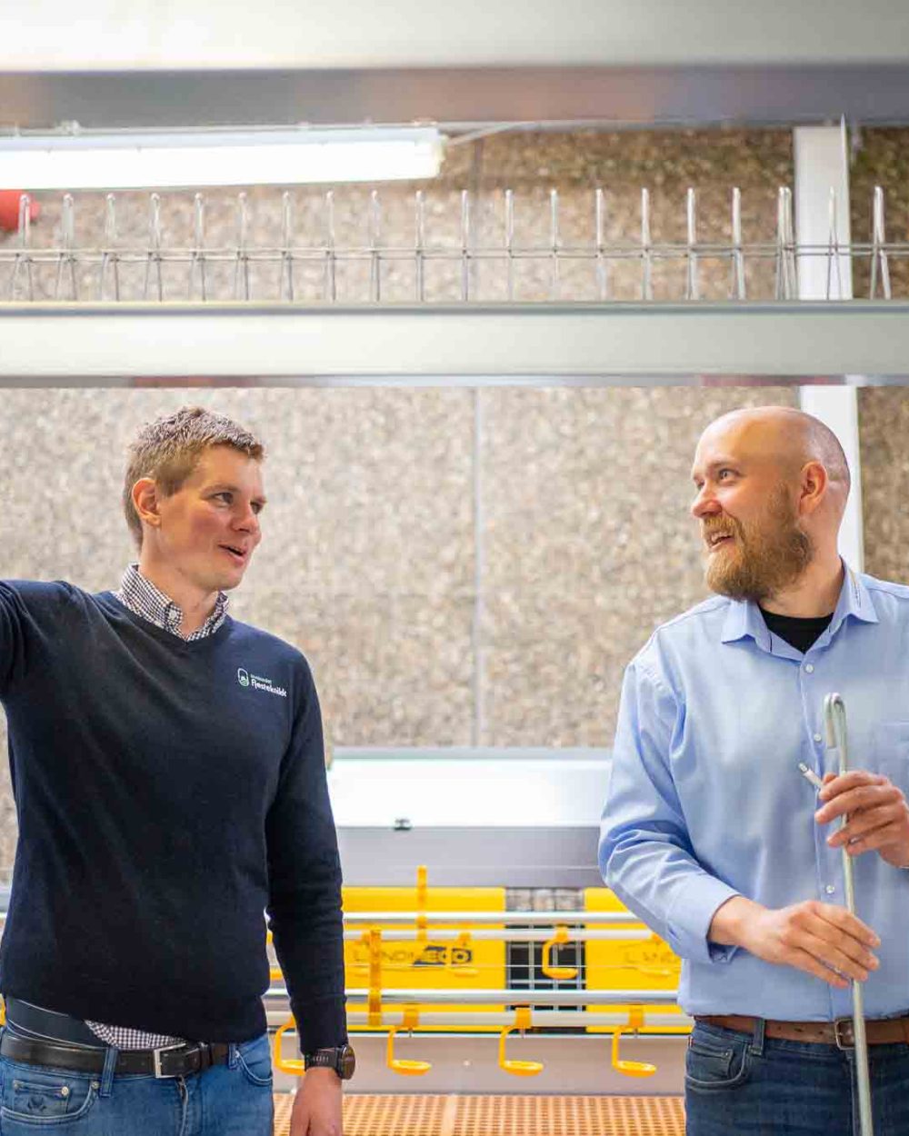 Two men in a professional setting discussing poultry rearing equipment, with LANDMECO systems in the background.