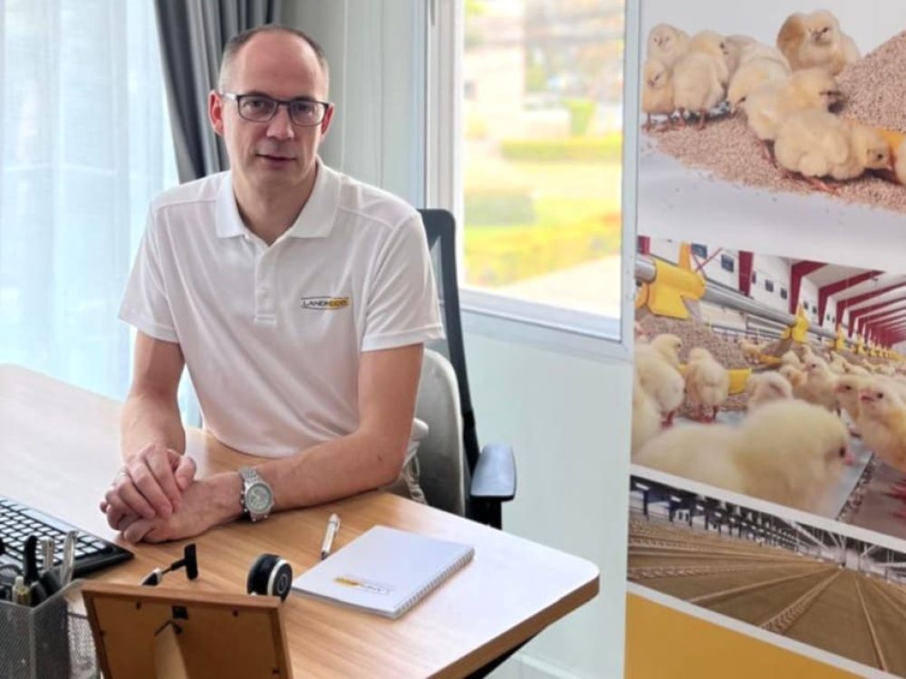 Frank Andreasen of LANDMECO at his desk, featuring poultry house and chick equipment graphics.