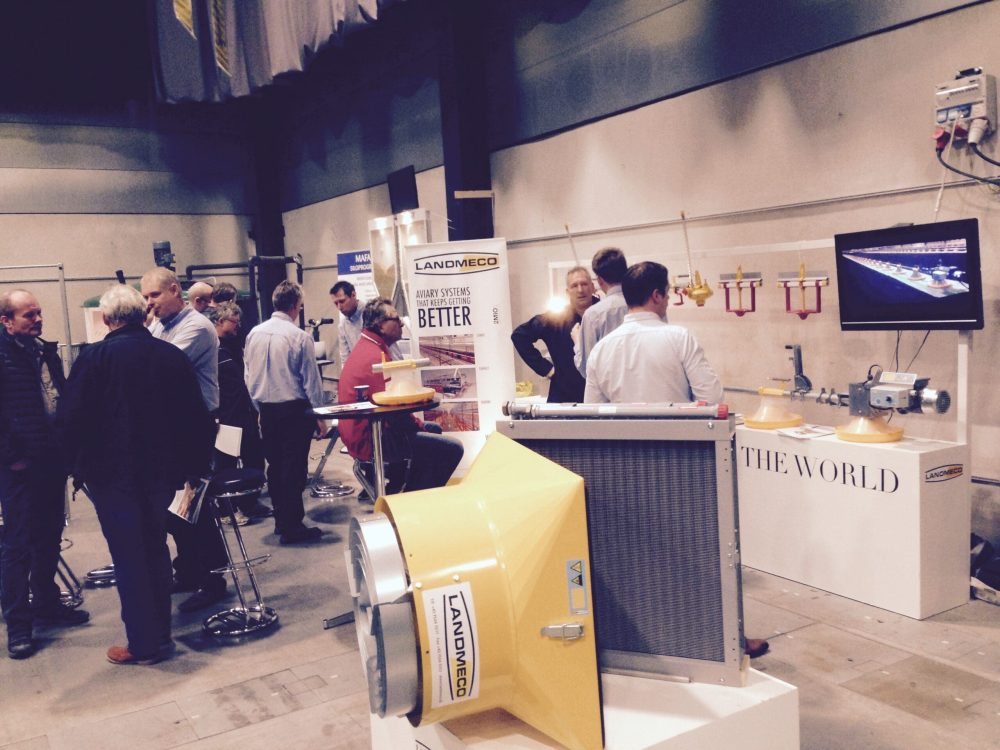 LANDMECO exhibition booth showing poultry feeding, ventilation, and aviary systems with staff talking to visitors.