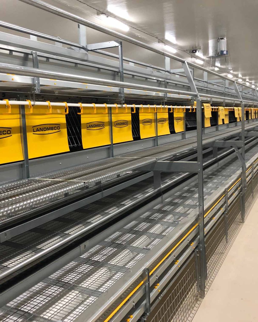 LANDMECO aviary system featuring metal tiers and yellow nesting flaps for cage-free poultry production.