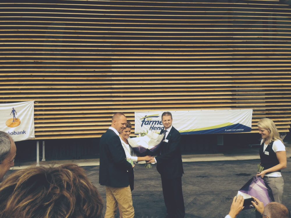 LANDMECO partners receiving flowers at a farming event with Rabobank and ForFarmers Hendrix banners in the background.