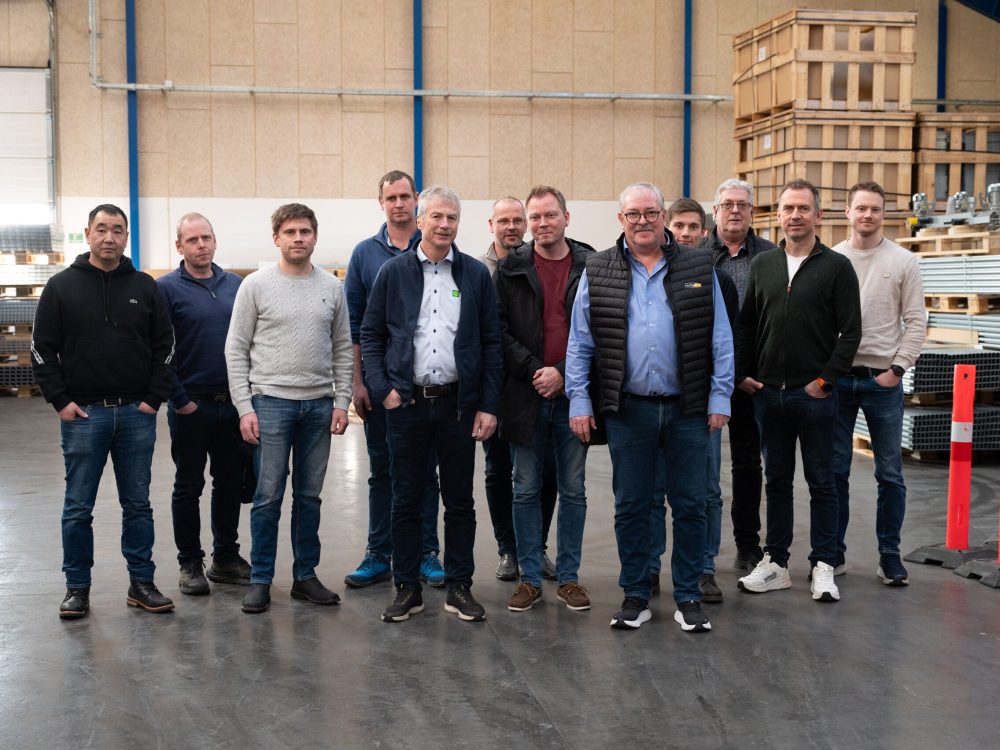 A group of professional men standing in a LANDMECO poultry equipment warehouse during a factory visit from Norway.