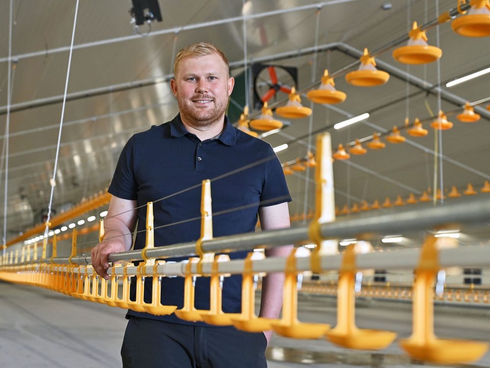 Mathias Højgaard står i sin nye, moderne kyllingestald i Vestjylland ved de gule fodringsanlæg.