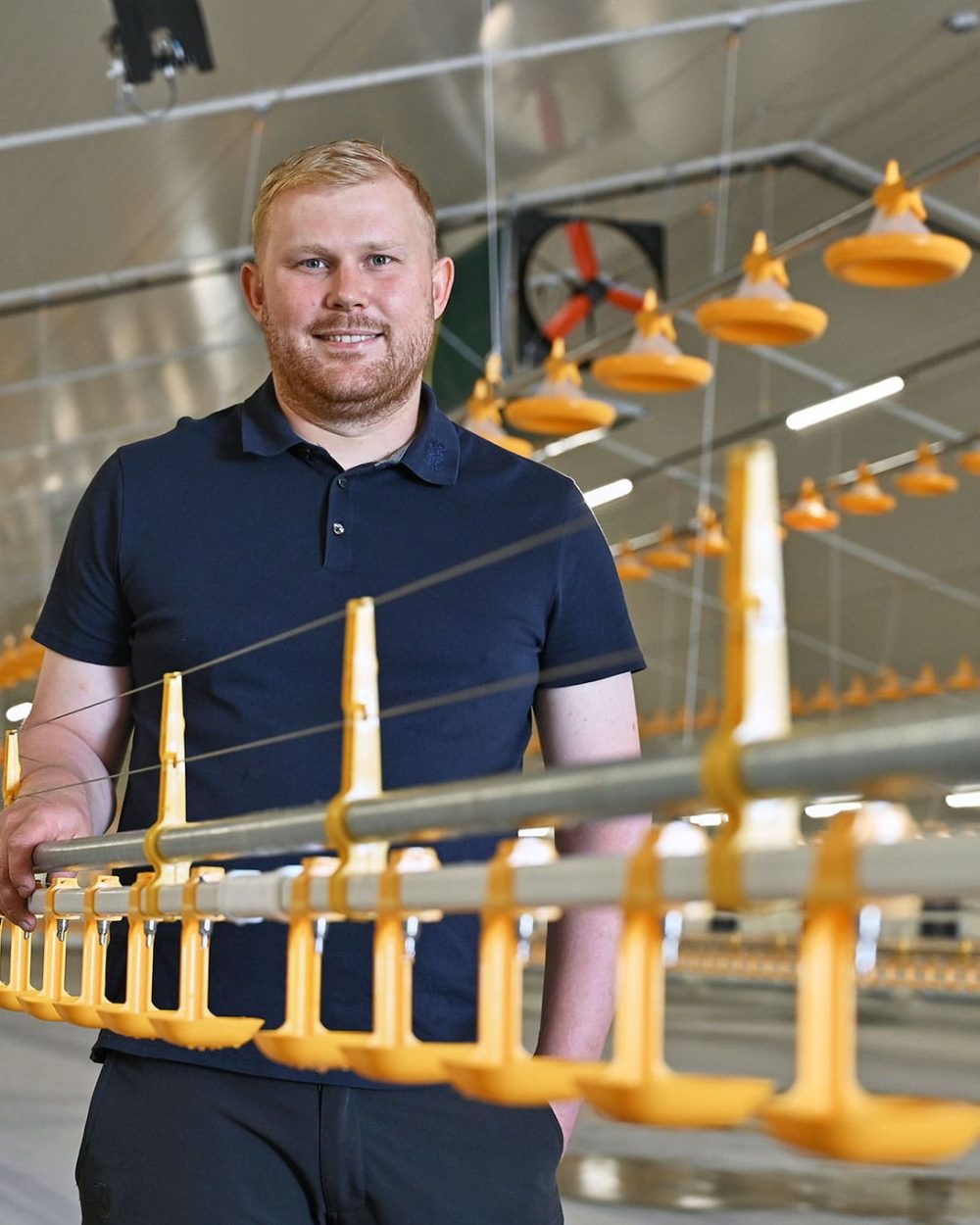 Mathias Højgaard står i sin nye, moderne kyllingestald i Vestjylland ved de gule fodringsanlæg.
