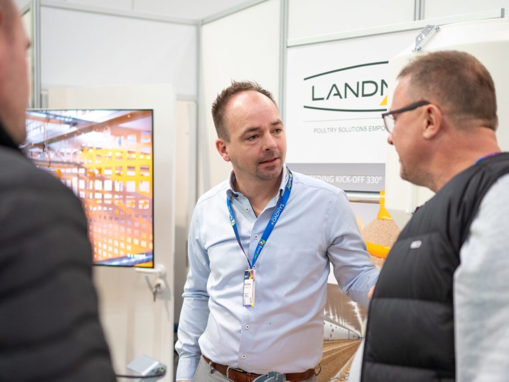 LANDMECO Sales Manager discussing poultry equipment with producers at a trade show.